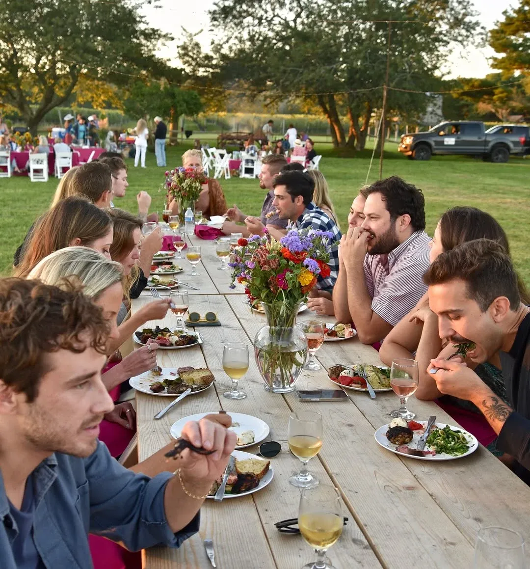 Guests sharing a meal at a long outdoor table with flowers and wine glasses