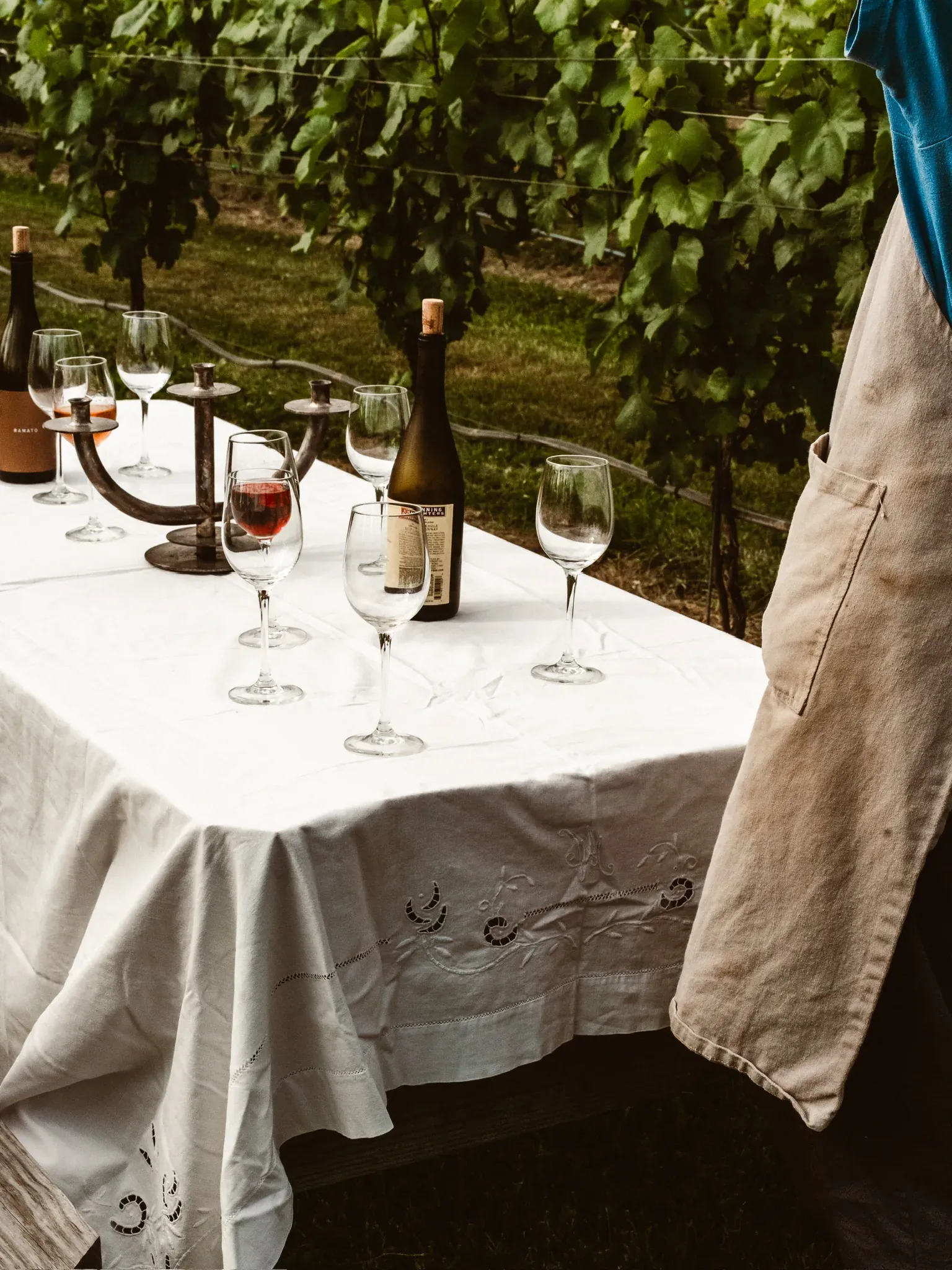 Glasses and a bottle on a white tablecloth, an apron at the edge of the frame
