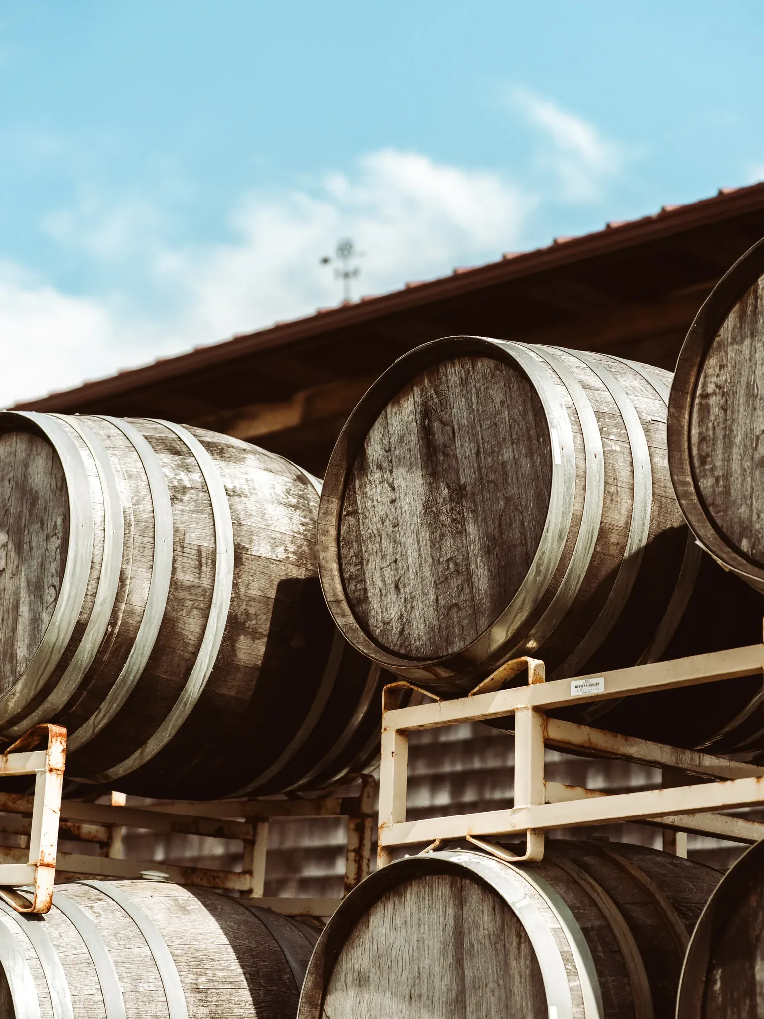 Oak barrels stacked on their sides in the shade of the barn