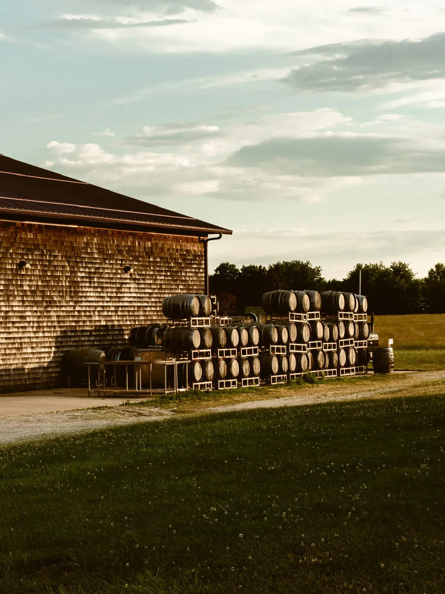 The shingled barn with barrels lined up along its wall, under a wide sky